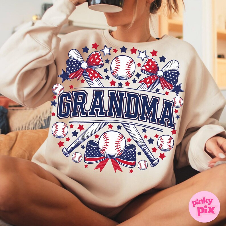 May include: A beige sweatshirt with a graphic design of two crossed baseball bats, baseballs, and red, white, and blue bows. The text "GRANDMA" is in the center of the design.