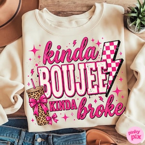 May include: A cream-colored crewneck sweatshirt featuring a graphic print with the text "kinda BOUJEE kinda broke" in pink and white. The design includes a leopard print tumbler with a pink bow, a pink and white checkered lightning bolt, and stars.