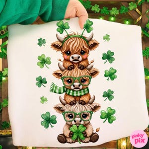 May include: White pillow featuring a stack of three cartoon Highland cows. The cows are brown and tan, wearing green glasses, scarves, and shamrock headbands. Green shamrocks are scattered around the cows.
