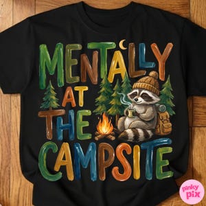 May include: Black t-shirt with the text "MENTALLY AT THE CAMPSITE" in colorful letters. A raccoon wearing a knit cap is sitting near a campfire, holding a mug. Trees and a backpack are also featured in the design.