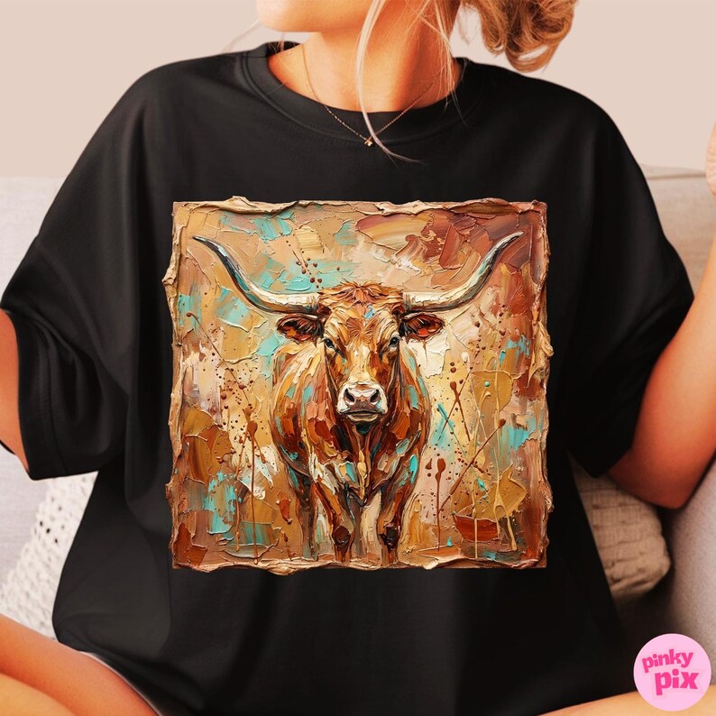 May include: Black t-shirt featuring a square, textured image of a longhorn steer. The steer is brown with long horns, set against a background of brown, teal, and gold paint strokes. The shirt is a casual style.