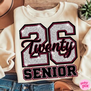 May include: Cream-colored sweatshirt with the number "26" in silver glitter and maroon trim. The word "Twenty" is in a script font, and "SENIOR" is printed below. The design is on the front of the sweatshirt.