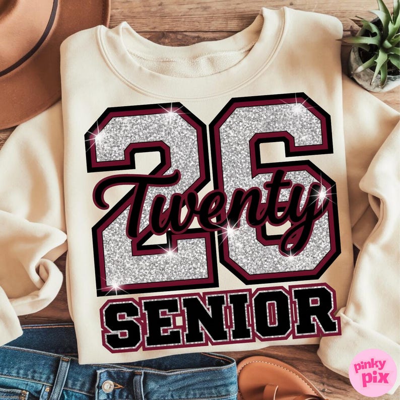 May include: Cream-colored sweatshirt with the number "26" in silver glitter and maroon trim. The word "Twenty" is in a script font, and "SENIOR" is printed below. The design is on the front of the sweatshirt.