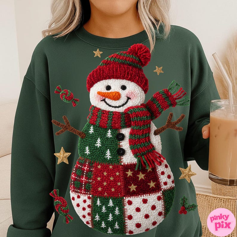 May include: A dark green sweatshirt featuring a whimsical snowman design. The snowman has a red knit hat and scarf, a carrot nose, and a patchwork body with green, red, and white squares. Gold star and candy accents surround the snowman.