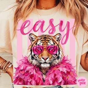 May include: Cream-colored t-shirt featuring a tiger wearing pink sunglasses and a pink feather boa. The word "easy" is written in pink script above the tiger. The design is set against a pink and white striped background.