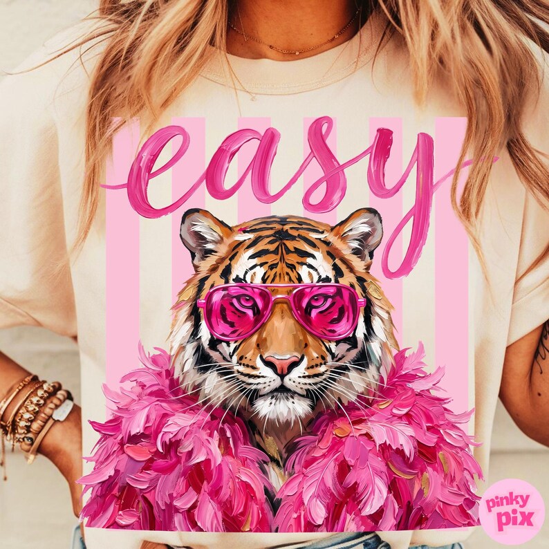 May include: Cream-colored t-shirt featuring a tiger wearing pink sunglasses and a pink feather boa. The word "easy" is written in pink script above the tiger. The design is set against a pink and white striped background.