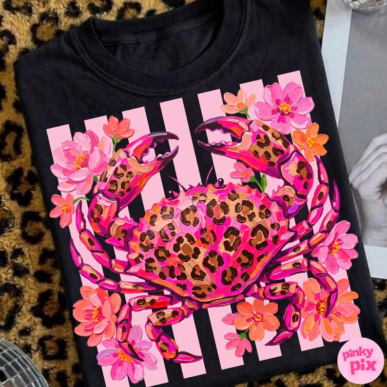 May include: Black crew neck t-shirt featuring a vibrant crab design. The crab has a leopard print pattern on its shell and claws, surrounded by pink and orange flowers. The background has pink stripes.