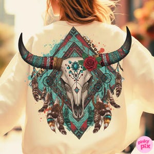 May include: Cream-coloured sweatshirt with a detailed graphic of a bull skull with long, curved horns. The design incorporates turquoise, red, and brown elements, including feathers, a rose, and geometric patterns. The overall theme is bohemian and southwestern.