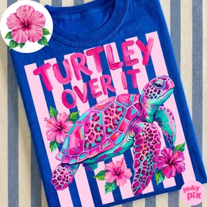 May include: Blue t-shirt with a vibrant graphic of a sea turtle and hibiscus flowers. The text "TURTLEY OVER IT" is displayed in pink. The turtle has a colorful shell with leopard print accents.