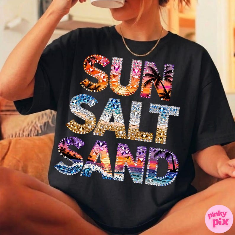 May include: Black t-shirt with the words "SUN SALT SAND" in a colorful, gem-like design. The letters are filled with images of sunsets, waves, and palm trees. The shirt is a casual, comfortable style.
