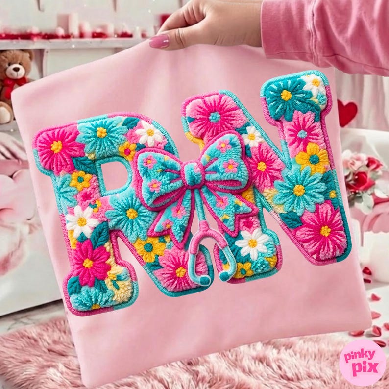 May include: Pink pillow with embroidered letters "RN" filled with colorful flowers. A bow and stethoscope are also embroidered. The letters are outlined in a teal color. The pillow is held by a person.