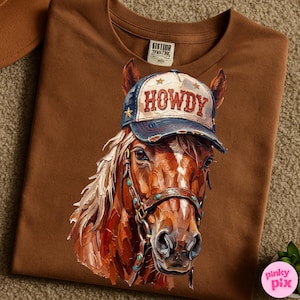 May include: Brown t-shirt featuring a detailed illustration of a horse wearing a blue and white baseball cap with the word "HOWDY" on it. The horse has a brown bridle with turquoise accents. The shirt has a tag that says "SISTIOR MOCHE".