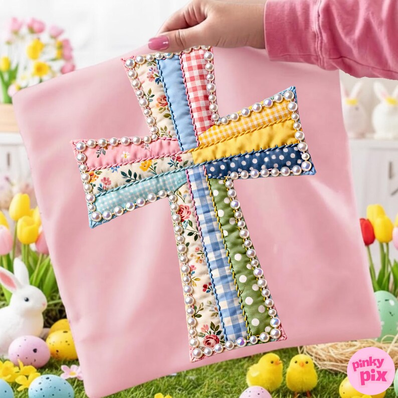 Op de afbeelding: Een roze stoffen kruis met een patchwork ontwerp met bloemen-, ruit- en stippenpatronen. Het kruis is omrand met kleine, witte parels. De afbeelding heeft een Paasthema, met eieren, kuikens en een konijn op de achtergrond.
