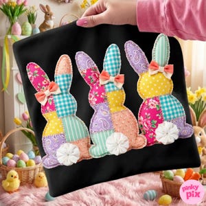 Könnte beinhalten: Schwarzer Stoff mit drei Patchwork-Hasen-Designs. Jeder Hase besteht aus verschiedenen gemusterten Stoffen, darunter Blumenmuster, Tupfen und Vichy, mit einer kleinen Schleife und einem weißen, flauschigen Schwanz. Die Hasen sind in einer Reihe angeordnet.