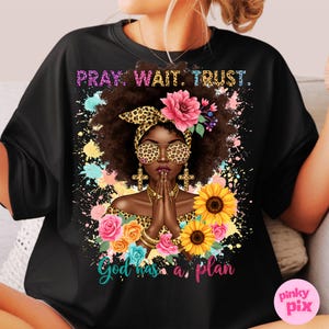 May include: Black t-shirt with a colorful illustration of a woman with a crown of flowers and the text "Pray. Wait. Trust. God has a plan."