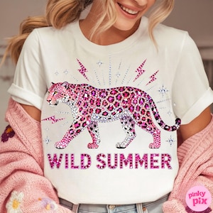 May include: White t-shirt featuring a pink leopard design with a rhinestone pattern. The leopard is surrounded by pink lightning bolts and stars. The words "WILD SUMMER" are printed in pink below the leopard.