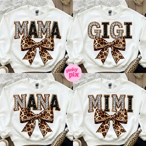 May include: White sweatshirts with rhinestone-studded text spelling "MAMA", "GIGI", "NANA", and "MIMI". Each sweatshirt features a leopard print bow. A pink circle with the text "pinky pix" is in the image.