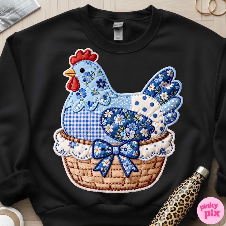 May include: Black sweatshirt featuring a patchwork design of a blue chicken in a woven basket. The chicken has floral and polka dot patterns. A blue bow adorns the basket. The design is detailed with red, white, and yellow accents.