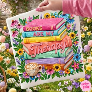 May include: A decorative square pillow featuring a stack of colorful books with the words "BOOKS ARE MY THERAPY." The design includes a coffee cup and is surrounded by flowers in a garden setting.