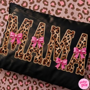 May include: Black decorative pillow with the word "MAMA" in leopard print letters outlined in gold glitter. Each letter has a pink bow. The pillow is on a pink and brown leopard print background.
