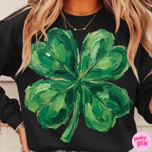 K&ouml;nnte beinhalten: Schwarzes Sweatshirt mit einem gro&szlig;en, strukturierten gr&uuml;nen vierbl&auml;ttrigen Kleeblatt-Design mit goldenen Akzenten. Das Kleeblatt ist mit sichtbaren Pinselstrichen gemalt, was einen k&uuml;nstlerischen Look erzeugt. Ein l&auml;ssiges Kleidungsst&uuml;ck, ideal f&uuml;r St. Patrick's Day.