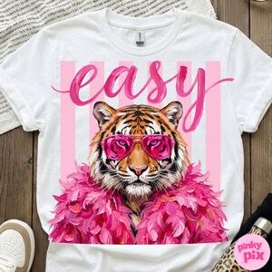 May include: White t-shirt featuring a tiger wearing pink sunglasses and a pink feather boa. The word "easy" is written in pink script above the tiger. Pink and white vertical stripes are behind the tiger.