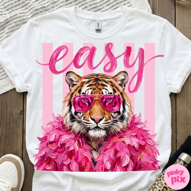 May include: White t-shirt featuring a tiger wearing pink sunglasses and a pink feather boa. The word "easy" is written in pink script above the tiger. Pink and white vertical stripes are behind the tiger.