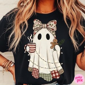 May include: Black t-shirt featuring a cartoon ghost with a festive bow, holding a coffee mug and gingerbread man. The ghost is adorned with patchwork and string lights, creating a cozy holiday theme.