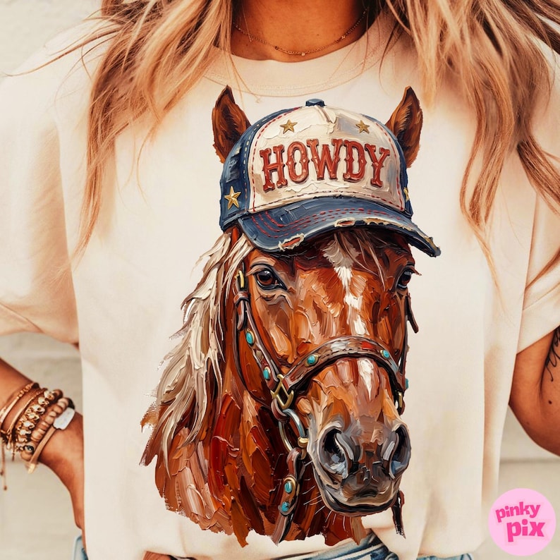 May include: A beige t-shirt featuring a detailed illustration of a brown horse wearing a blue and white baseball cap with the word "HOWDY" on it. The horse has a bridle with turquoise accents.
