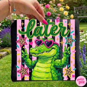 May include: A black square towel with a vibrant graphic featuring a green alligator wearing heart-shaped sunglasses and giving a peace sign. The word "Later" is written in green script above the alligator, with pink and black striped background.
