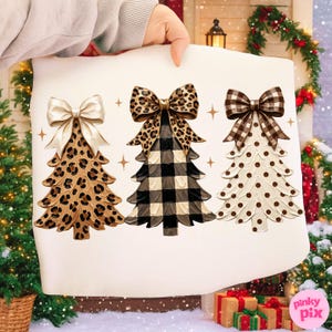 May include: A white fabric surface featuring a graphic print of three stylized Christmas trees. The first tree has a leopard print pattern with a cream bow, the second has a black and white buffalo check pattern with a leopard print bow, and the third has a white and brown polka dot pattern with a brown and white buffalo check bow.