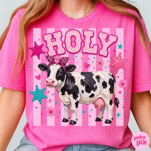 May include: A pink t-shirt featuring a cartoon cow with a leopard print bow and the word "HOLY" in pink letters. The design includes pink stars, hearts, and flowers, set against a striped background.