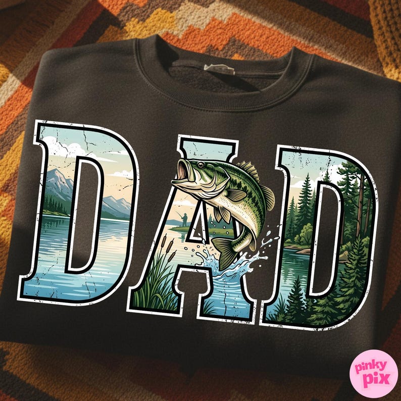 Pu&ograve; includere: Felpa nera con la scritta "DAD" in un font stilizzato. Le lettere sono riempite con una scena lacustre, un pesce che salta e una foresta. Il disegno ha un contorno bianco. La felpa &egrave; su una superficie a fantasia.