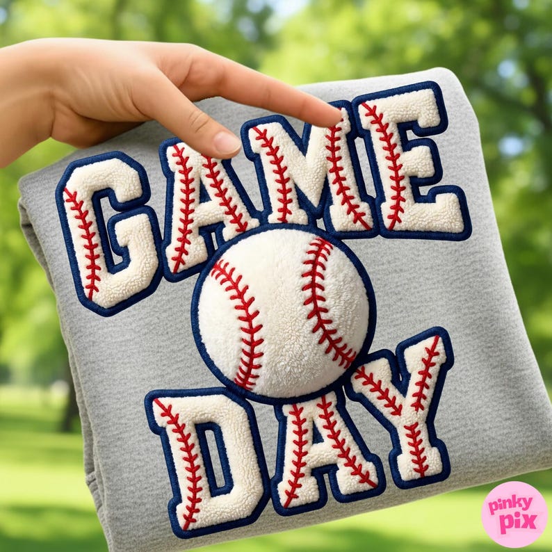 May include: A gray sweatshirt with the words "GAME DAY" in white, outlined in navy blue, and stitched with red thread to resemble baseball stitching. A baseball is centered on the sweatshirt. The Pinky Pix logo is in the bottom right corner.