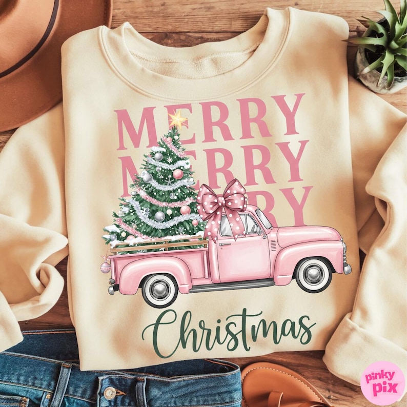 May include: Cream-colored sweatshirt with a pink Christmas truck graphic. The truck carries a decorated Christmas tree and a large bow. The words "MERRY CHRISTMAS" are printed in pink and green.