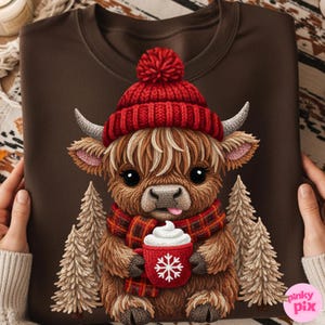 May include: Brown sweatshirt featuring a cartoon Highland cow wearing a red knit hat and scarf. The cow is holding a red mug with a snowflake design and whipped cream. Two stylized Christmas trees flank the cow.