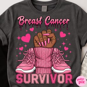 May include: Dark gray t-shirt with a pink graphic supporting breast cancer awareness. The design includes the words "Breast Cancer" and "Survivor", a raised fist, pink hearts, and pink sneakers.