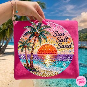 May include: A hot pink beach bag with a circular design featuring a sunset, palm trees, and the words "Sun Salt Sand." The design is embellished with sparkling crystals. The bag is held by a person with a bracelet.