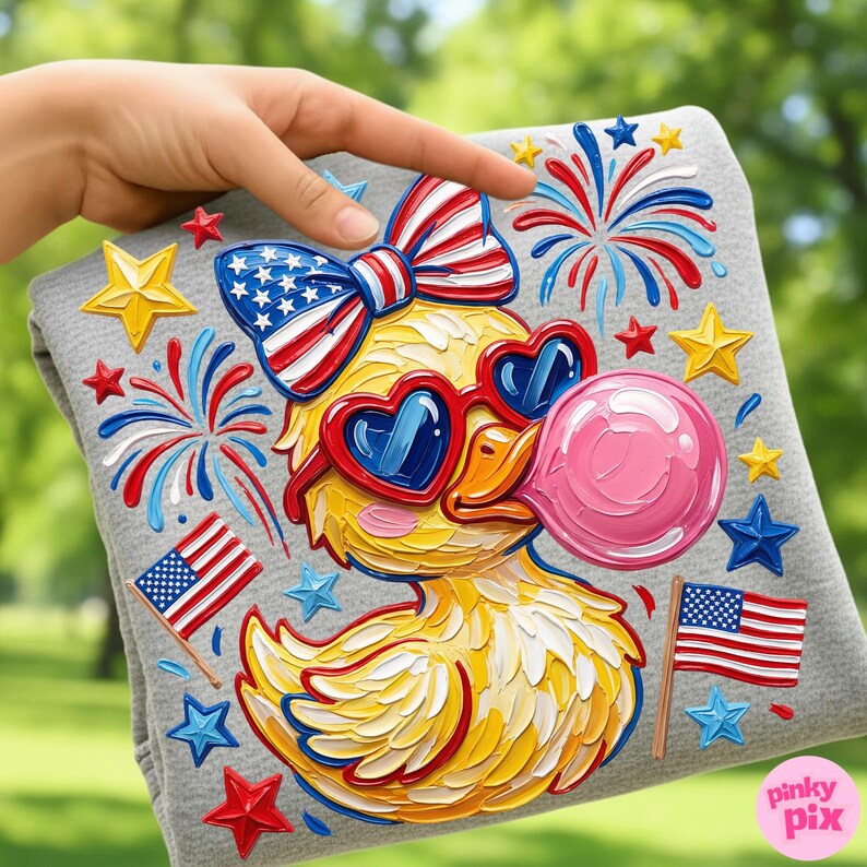 May include: A gray sweatshirt featuring a cartoon duck wearing heart-shaped sunglasses and a patriotic bow. The duck is blowing a pink bubble and surrounded by fireworks, stars, and American flags. The design has a textured, painted appearance.