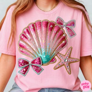 May include: Pink t-shirt featuring a sequined seashell design with pink and teal hues, adorned with pearls and rhinestones. Two sequined bows and a rhinestone starfish complete the design. The text "pinky pix" is in the bottom right corner.