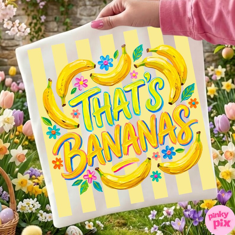 Pu&ograve; includere: Un cuscino bianco con strisce verticali gialle e la frase "THAT'S BANANAS" in lettere colorate. Il cuscino presenta illustrazioni di banane gialle, fiori blu e rosa e foglie verdi. Il cuscino &egrave; tenuto da una persona.