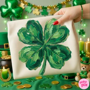 K&ouml;nnte beinhalten: Eine cremefarbene Leinwandtasche mit einem gro&szlig;en, strukturierten vierbl&auml;ttrigen Kleeblatt, das in Gr&uuml;nt&ouml;nen gemalt ist. Das Bild ist vor einem Hintergrund zum Thema St. Patrick's Day mit Goldm&uuml;nzen, Kleebl&auml;ttern und einem Teddyb&auml;ren platziert.