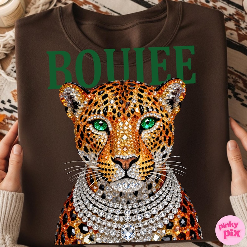 May include: Brown sweatshirt featuring a jeweled leopard design with emerald green eyes and a diamond necklace. The word "BOHIEE" is printed in green at the top. The design is centered on the front of the sweatshirt.