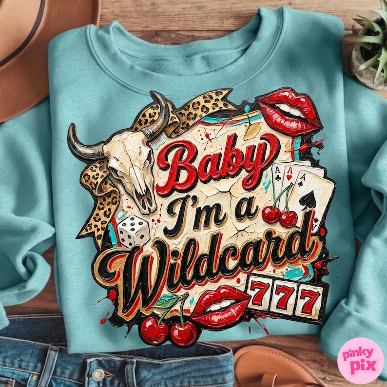 Może przedstawiać: Jasnoniebieska bluza z nadrukiem graficznym. Projekt zawiera czaszkę byka, karty do gry, kości, wiśnie oraz napis "Baby I'm a Wildcard" w kolorze czerwonym i czarnym. Widnieje r&oacute;wnież liczba 777.