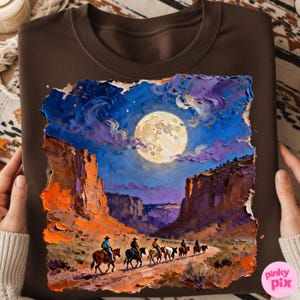 May include: Brown crewneck sweatshirt featuring a vibrant, textured painting of a desert landscape under a full moon. Cowboys on horseback ride along a path between towering rock formations, under a starry night sky.