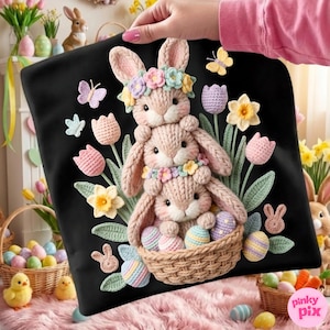 Può includere: Cuscino nero con una coppia di coniglietti lavorati a maglia impilati che indossano corone di fiori, circondati da fiori e farfalle lavorati a maglia. Il coniglietto in basso tiene un cestino di uova di Pasqua dai colori pastello. Un affascinante tema pasquale.