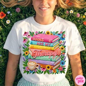 May include: White t-shirt featuring a colorful graphic of stacked books with the words "Books Are My Therapy." The design includes a coffee cup and is surrounded by flowers. The shirt is a casual wear item.