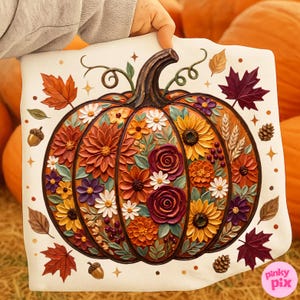 Puede incluir: Un cojín decorativo con un diseño detallado de calabaza. La calabaza está llena de varias flores en tonos naranja, amarillo y morado. Hojas de otoño, bellotas y piñas rodean la calabaza, creando un tema otoñal.