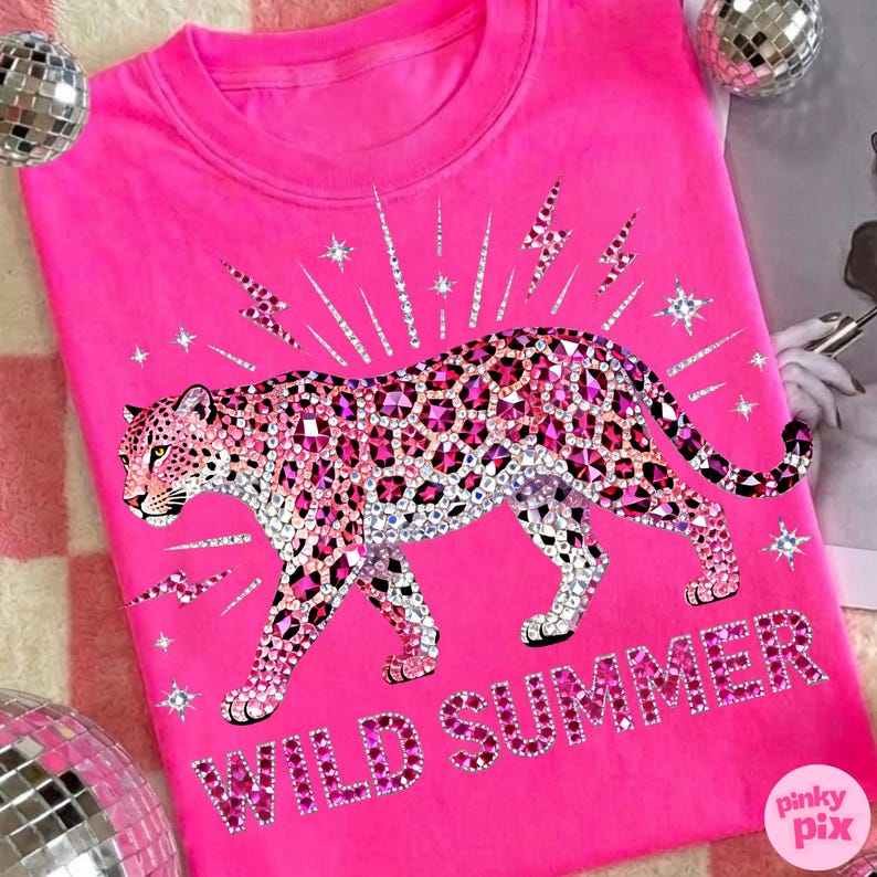 May include: A bright pink sweatshirt featuring a bedazzled leopard design with pink and clear rhinestones. The words "WILD SUMMER" are spelled out in pink rhinestones below the leopard. The design includes lightning bolts and stars.
