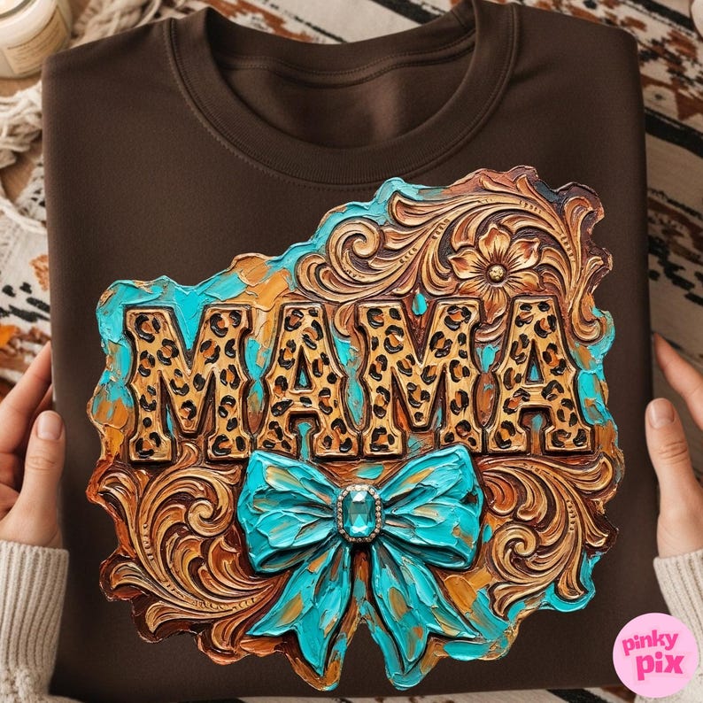 May include: A brown sweatshirt featuring a decorative design with the word "MAMA" in leopard print. The design includes a turquoise bow with a jewel and ornate, carved details in shades of brown and gold.